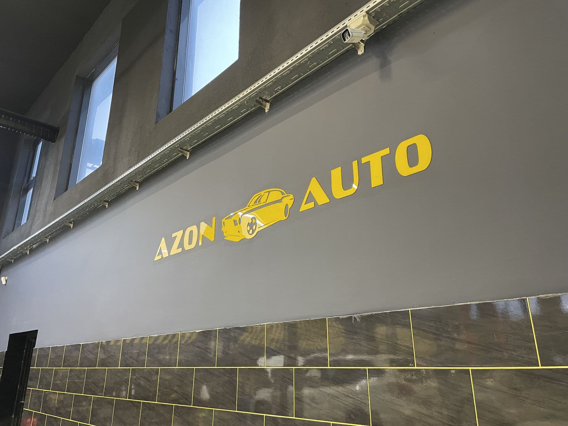 Servis divarında sarı AZON AUTO loqosu və nəzarət kamerası