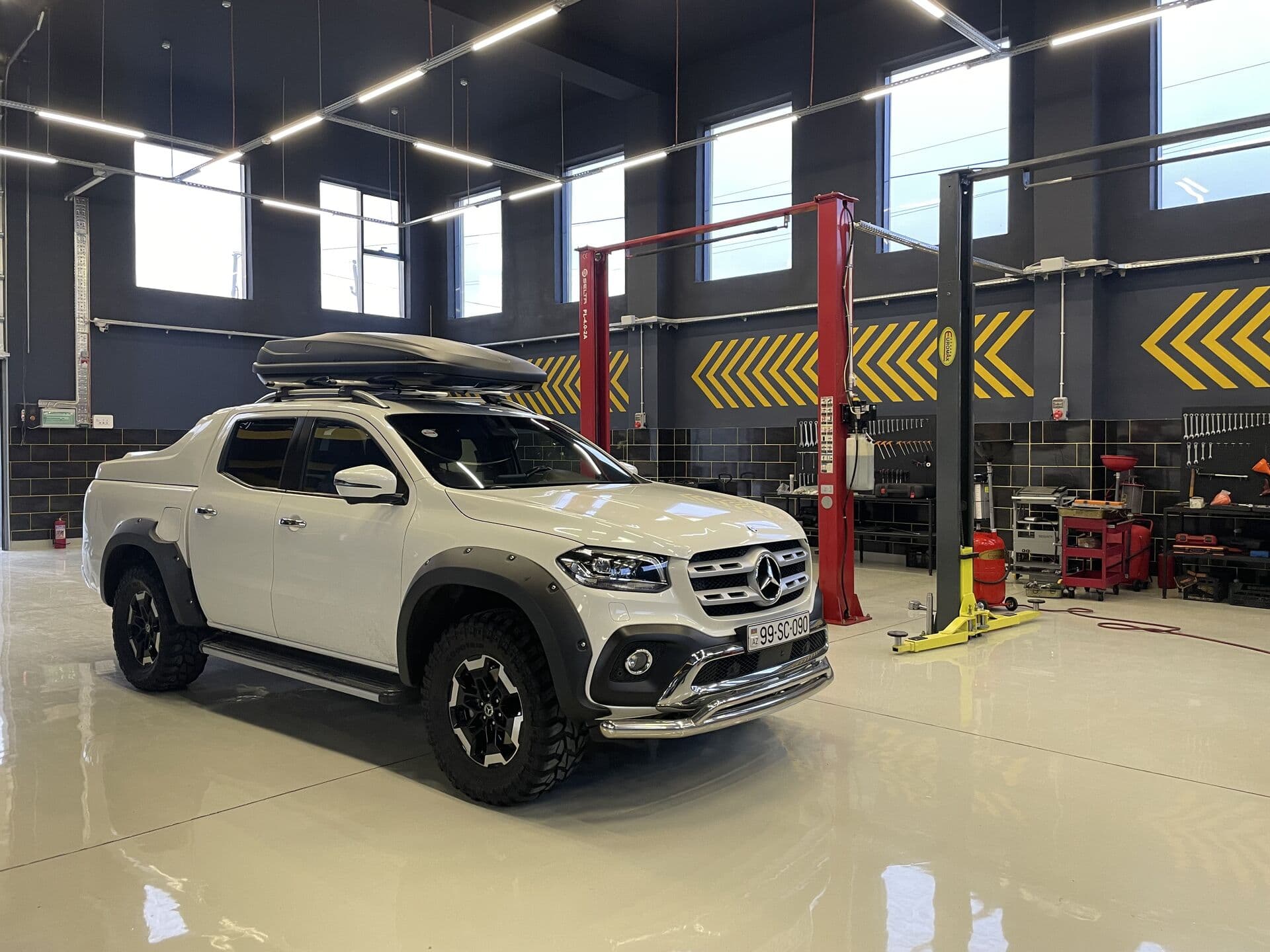 Təmir zalında ağ Mercedes-Benz X-Class pikap, arxada iki dirəkli qaldırıcılar və alət arabaları, AzonAuto, Bakı