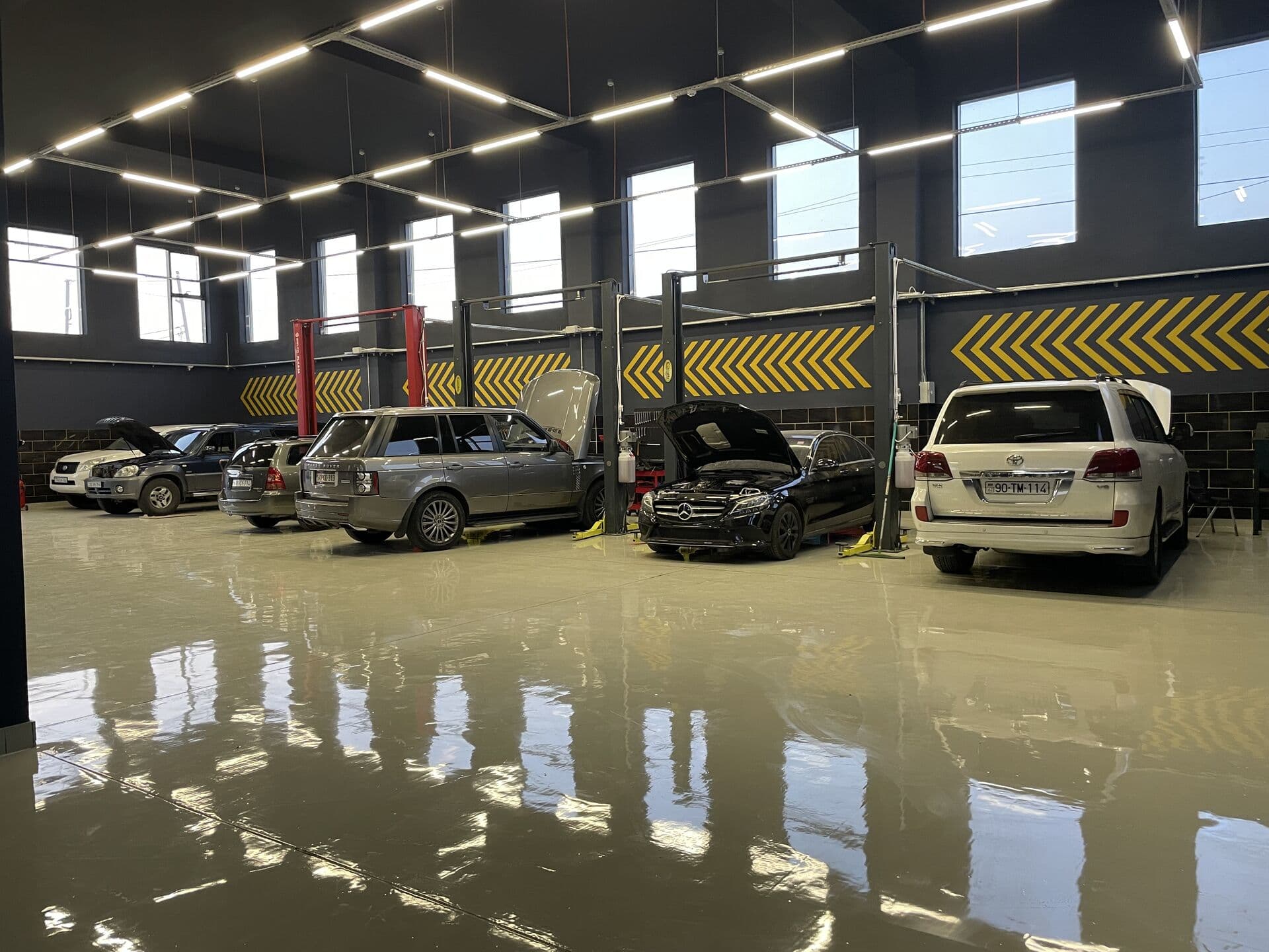 AzonAuto-nun təmir zalı: qaldırıcılar arasında kapotu açıq Range Rover və Mercedes-Benz C-Class, ağ Toyota Land Cruiser, Bakı