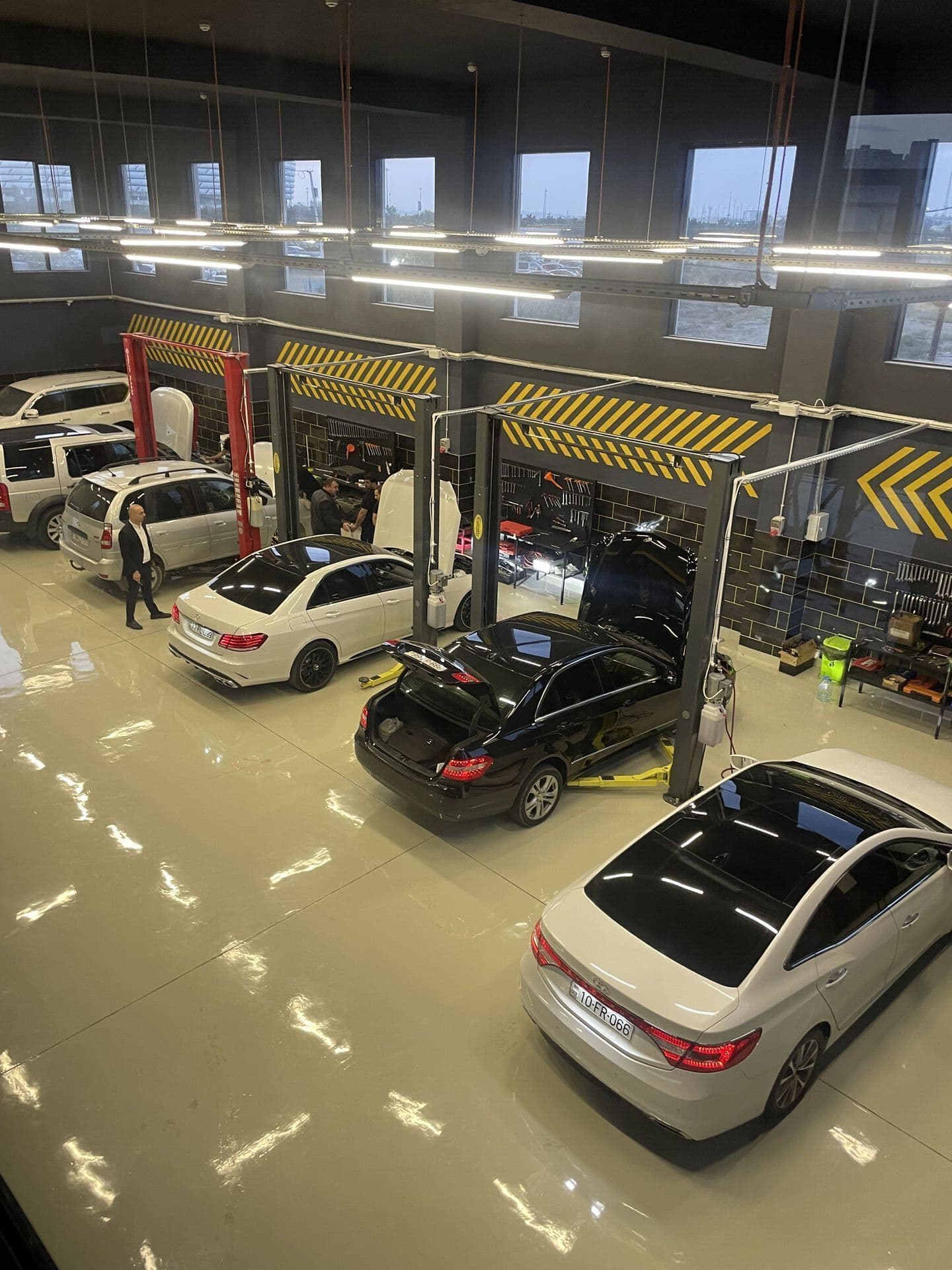 Təmir zalına yuxarıdan baxış: qaldırıcılar arasında ağ və qara Mercedes-Benz sedanlar, önündə ağ sedan, AzonAuto, Bakı