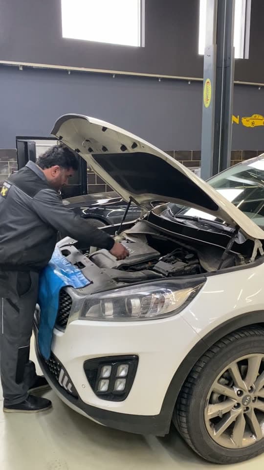 Ağ Kia Sorento-nun kapotu açıqdır, usta mühərrik bölməsində işləyir; zəncir dəsti dəyişilir, farsunkalar Common Rail stendində yoxlanır, kollektor təmizlənməzdən əvvəl və sonra göstərilir.