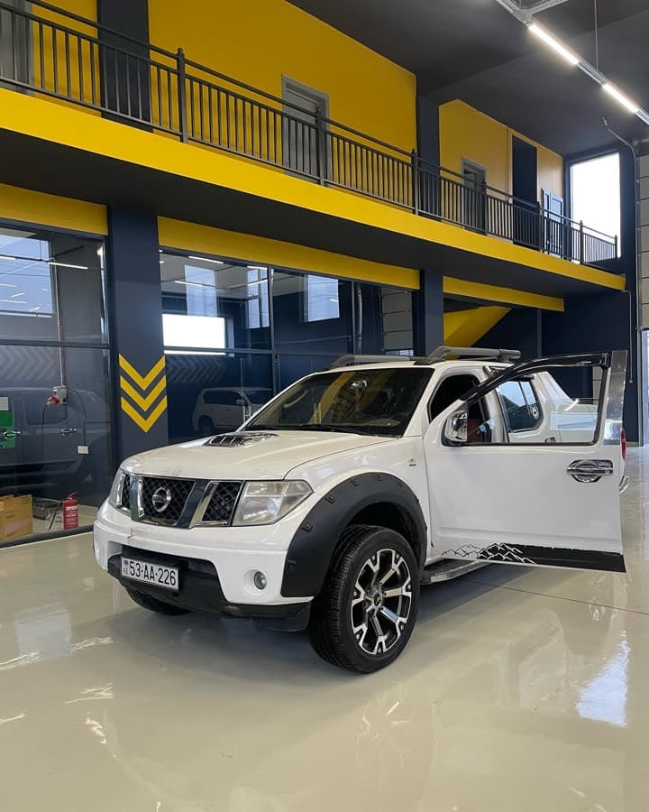Ağ Nissan Navara pikap AzonAuto-nun təmir zalında, qapısı açıq