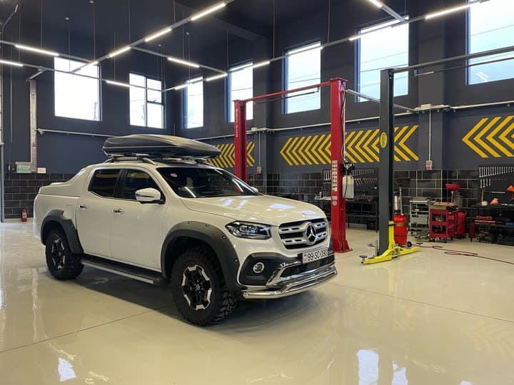 Ağ Mercedes-Benz X-Class pikap AzonAuto-nun təmir zalında, qaldırıcıların arasında